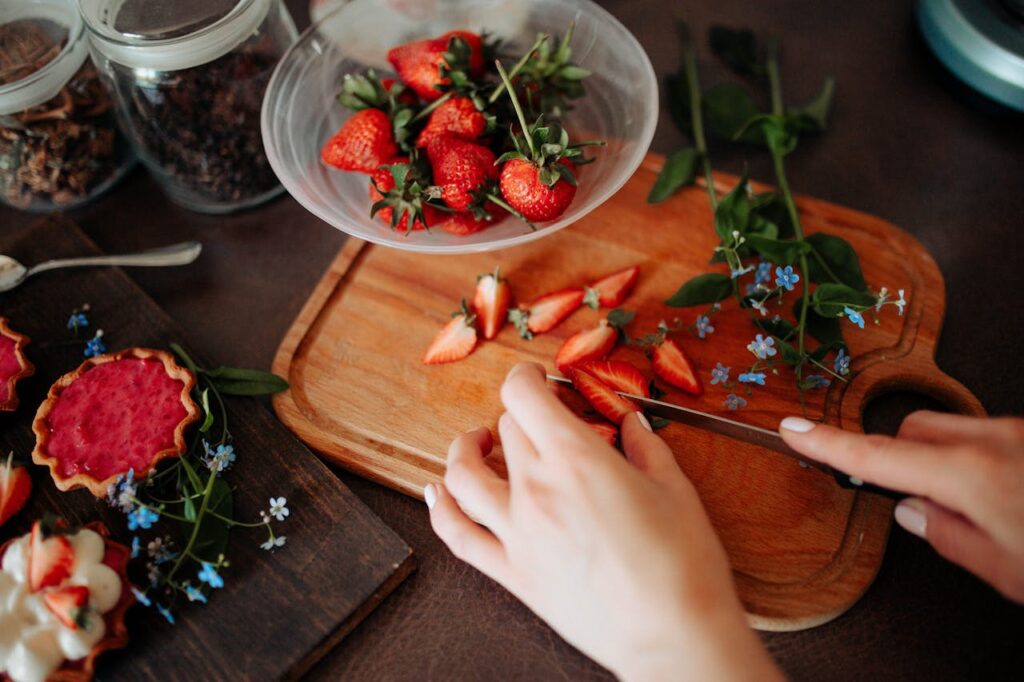 Hands slicing fresh strawberries on a wooden board, perfect for culinary projects.
